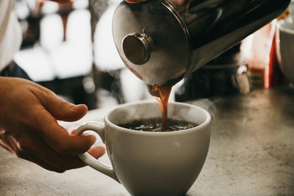 someone pouring french press coffee into a white coffee mug