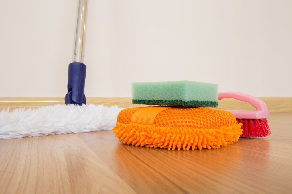 a mop, sponge, and brush on a wooden floor