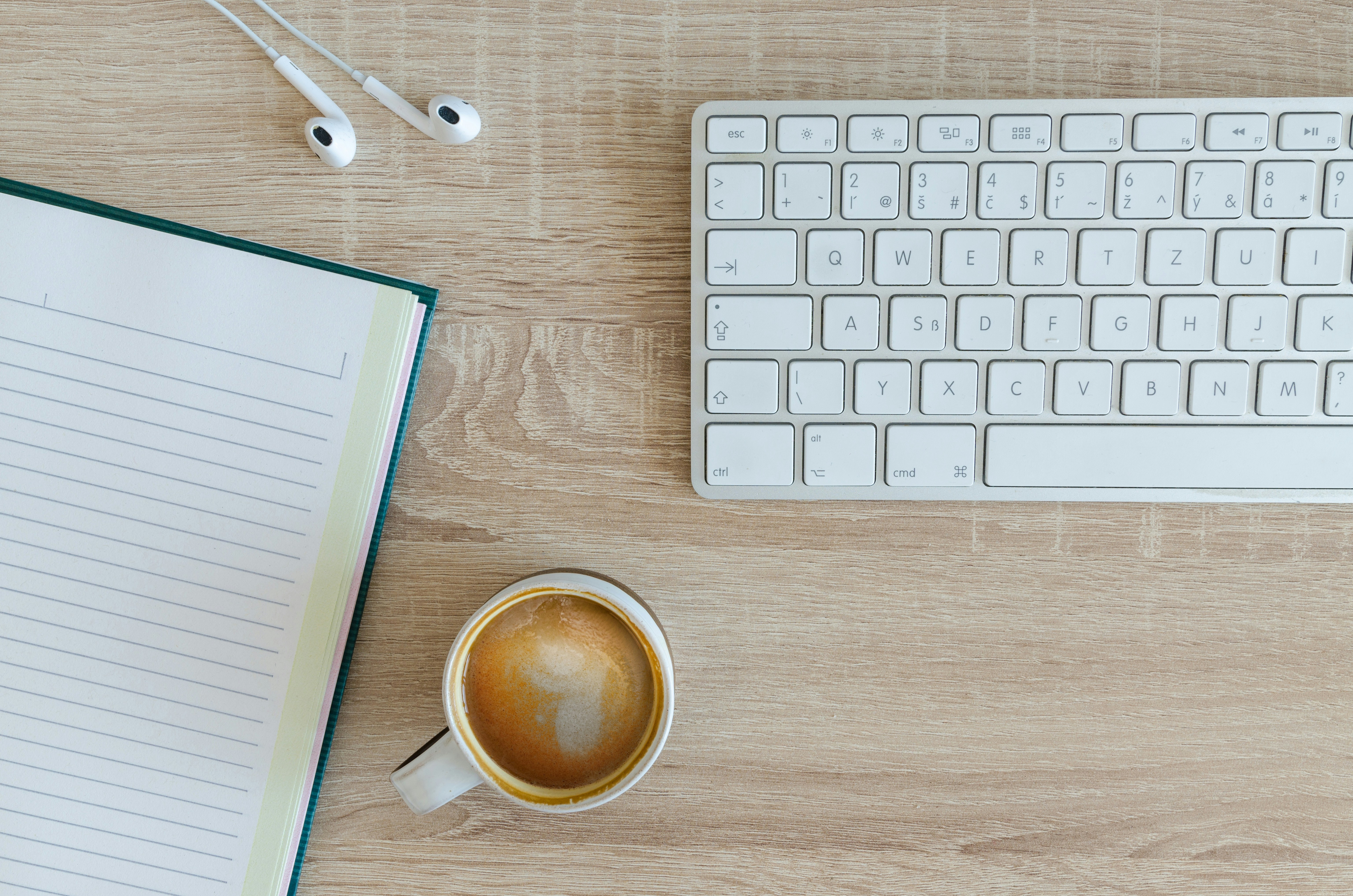 a notebook, coffee, and keyboard on a wooden desk