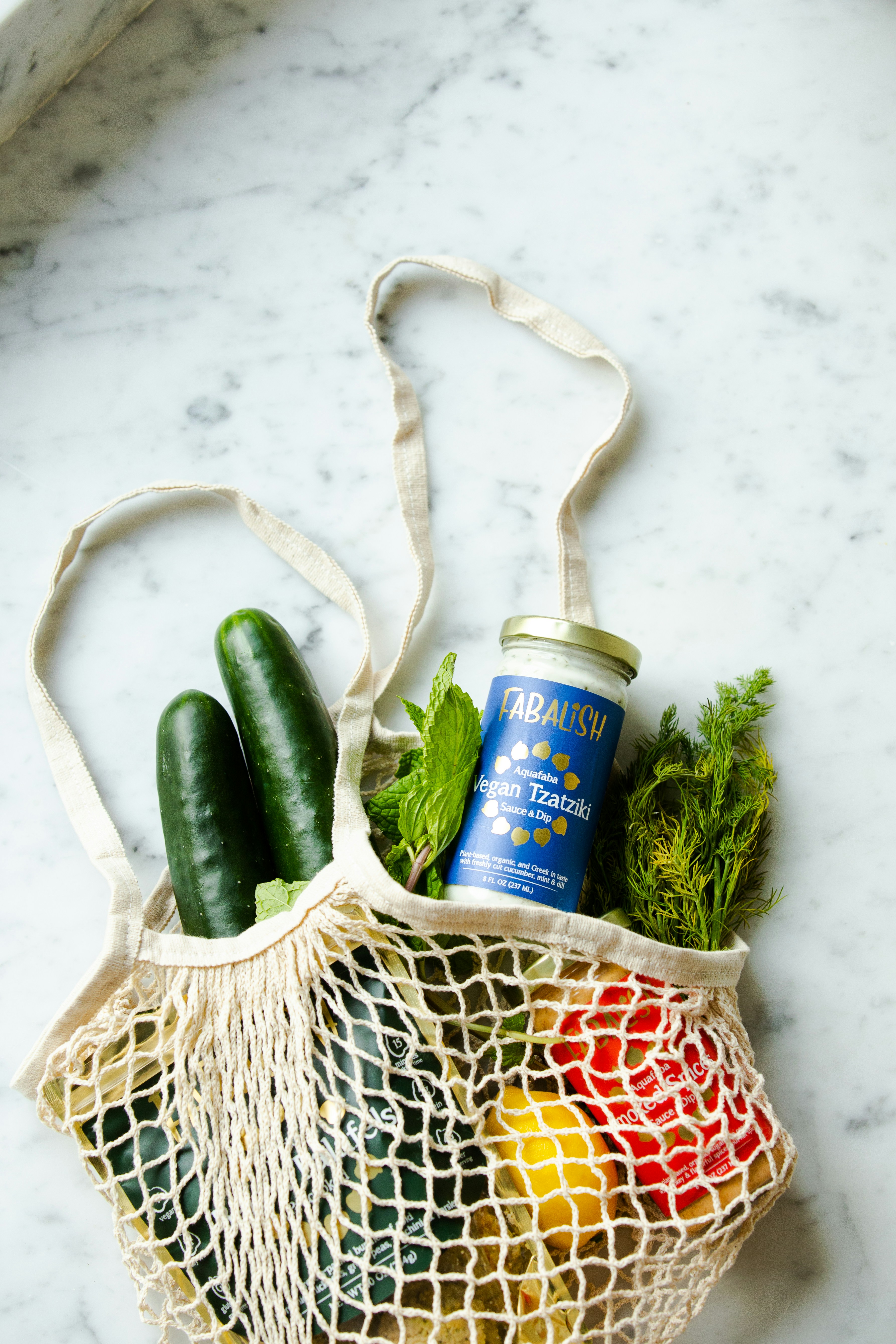 fabric grocery bag with cucumbers, dill, basil, lemon, tzatziki, and other grocery items in it