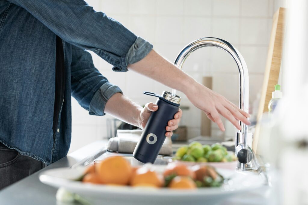 a person filling up their reusable water bottle at the sink